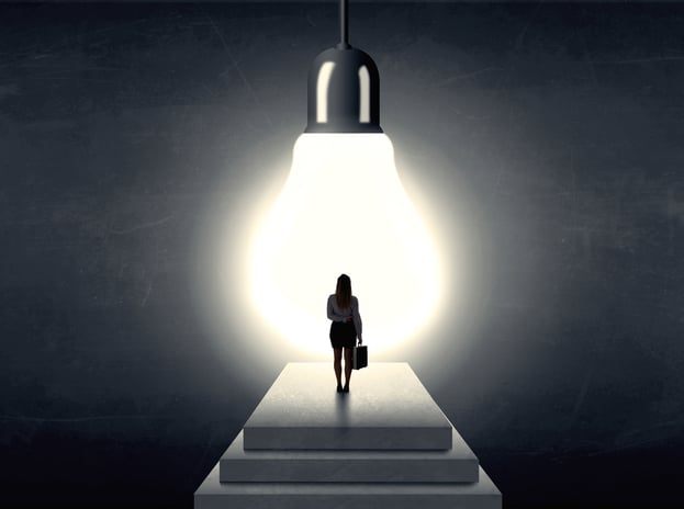 Businesswoman standing on a step in front of a huge light bulb, concept of having an idea.