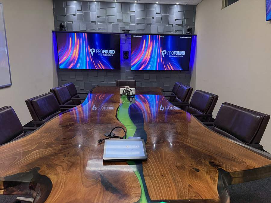 A modern conference room with a polished wooden table, chairs, and dual-mounted displays showing the Profound Technologies logo.