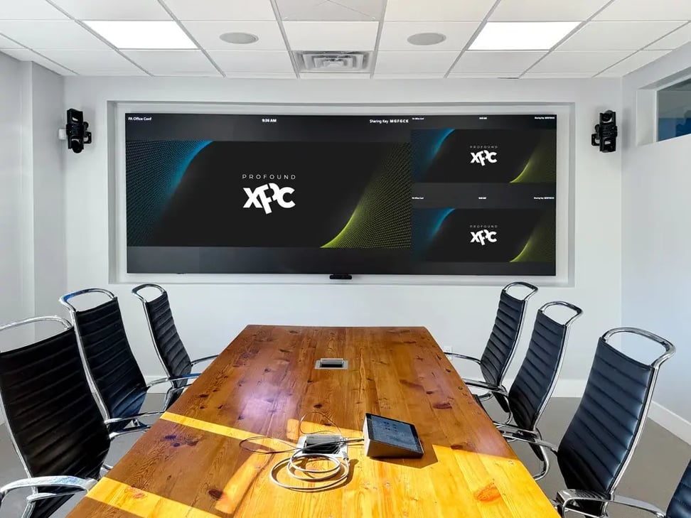 Conference room with a large video wall display, wall-mounted cameras, ceiling speakers, and a meeting table.