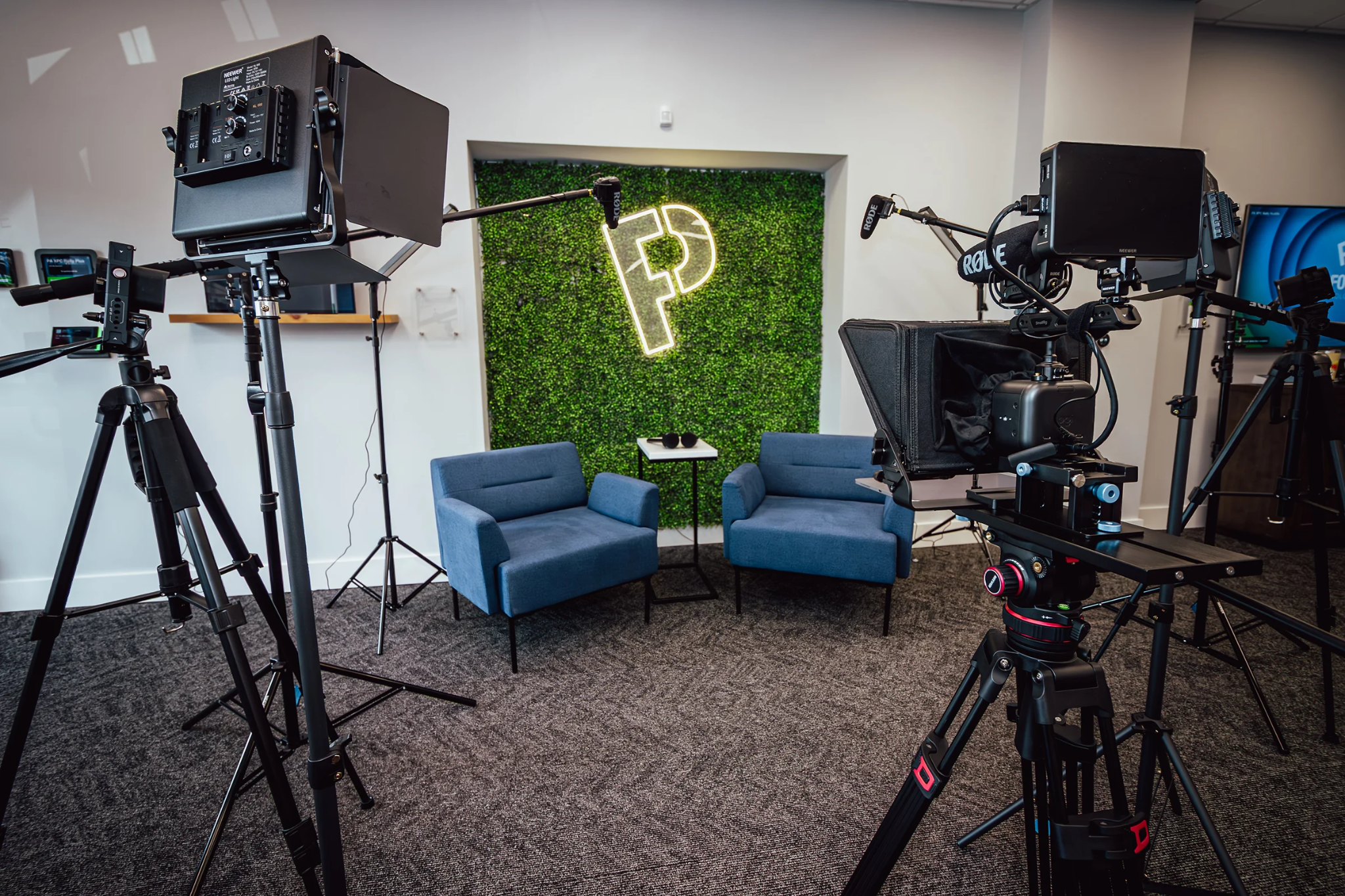 Video production studio with cameras, microphones, teleprompters, and two blue chairs.